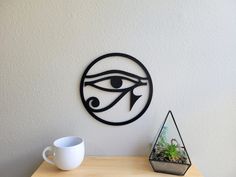 an eye is on the wall next to a coffee cup and terrarium in front of it