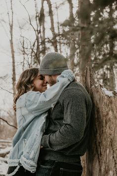 a man and woman standing next to each other in front of a tree trunk with snow on the ground