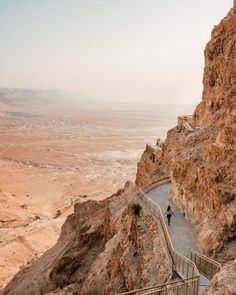 two people are walking up the stairs on top of a rocky cliff in the desert