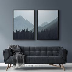 two paintings hang on the wall above a couch in front of a grey wall with mountains and trees