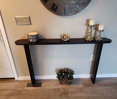 a black console table with two candles on it and a potted plant next to it