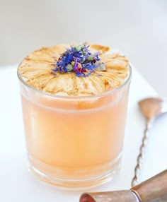 a small glass filled with liquid next to a metal spoon and flower on the side