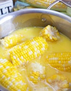 corn on the cob being cooked in a pot with broth and white sauce