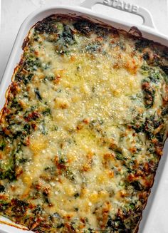 a casserole dish with cheese and spinach in it on a white surface