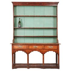 an old wooden bookcase with two drawers and a wine bottle on the top shelf