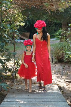 two women in red dresses walking down a wooden walkway with flowers on their head and one holding the hand of another woman's hand