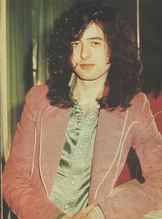 a man with long hair wearing a pink jacket and green tie