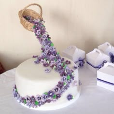 a white cake with purple and green flowers on it sitting on a table next to boxes