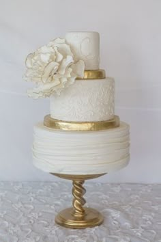 a three tiered cake with white frosting and gold accents on a tablecloth