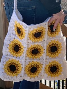 a woman is holding a crocheted bag with sunflowers on the front