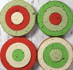 four green, red and white donuts sitting on top of a wooden table next to each other