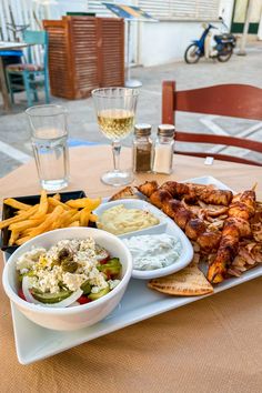 there is a plate with chicken wings, fries and dips next to wine glasses on the table