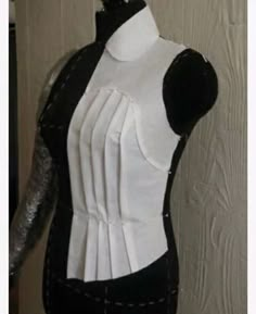 a mannequin with black and white material on it's back, sitting next to a wooden wall