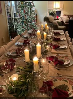 a table set for christmas dinner with lit candles and greenery on the centerpiece