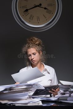 a woman sitting at a desk with papers in front of her and a clock above her