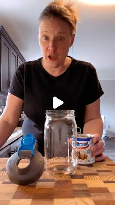 a woman sitting at a kitchen table with a jar of food in front of her