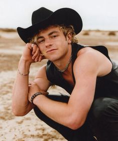 a young man wearing a cowboy hat and black leather outfit poses for a photo in the desert