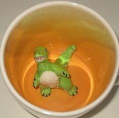 a green toy turtle floating in a cup of orange liquid