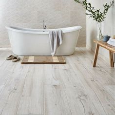 a white bath tub sitting on top of a wooden floor next to a table and chair