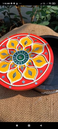 a red and yellow plate sitting on top of a brown cloth covered table next to plants