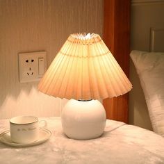 a table lamp sitting on top of a bed next to a cup and saucer