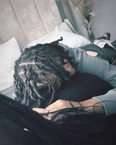 a man with dreadlocks laying on top of a bed next to a pillow