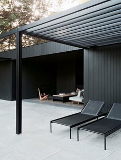 two black lounge chairs sitting on top of a cement floor next to a covered patio