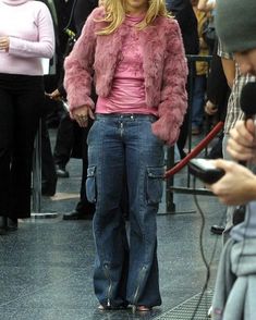 a woman in pink jacket and jeans standing next to a man holding a cell phone