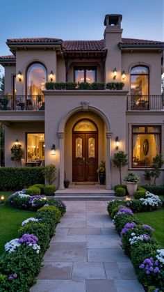 a large house with lots of windows and plants in the front yard at night time