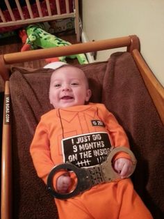 a baby in an orange shirt is holding a pair of scissors and smiling at the camera