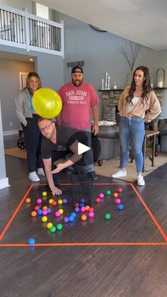 a group of people in a living room playing with some balls on the floor and one man holding a yellow balloon