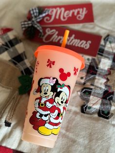 a plastic cup with mickey and minnie mouse on it sitting on a bed next to christmas decorations