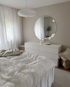 a white bed sitting under a round mirror in a bedroom