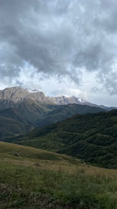 the mountains are covered in green grass and snow capped peaks under a cloudy blue sky