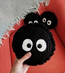 someone is holding up a crocheted black object with eyes