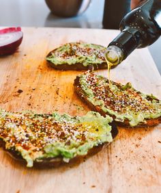 an avocado toast being drizzled with olive oil on a cutting board