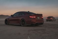 two cars are parked in the desert at dusk, one is red and the other is black