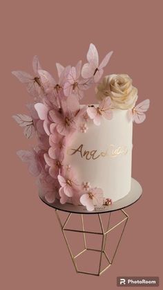 a white cake with pink flowers and gold lettering on top, sitting on a wire stand