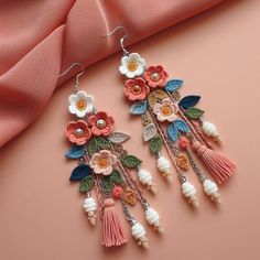 two pairs of earrings with flowers and tassels hanging from them on a pink background