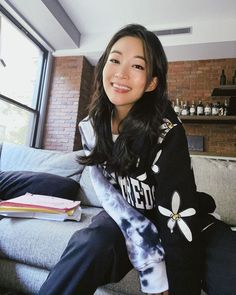 a woman is sitting on a couch smiling at the camera while wearing a tie dye sweatshirt