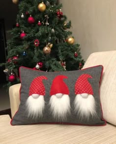 a christmas pillow with three gnomes on it sitting in front of a christmas tree