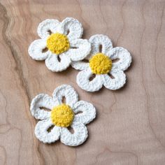 three crocheted white and yellow flowers sitting on top of a wooden table next to each other