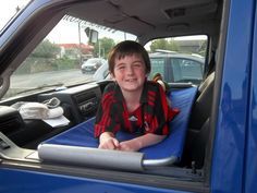 a young boy sitting in the back seat of a blue truck with his laptop open