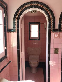 a pink bathroom with black and white tiles on the walls, an arched doorway leading to a toilet