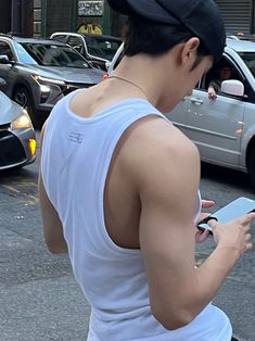 a man wearing a white tank top is looking at his cell phone in the street