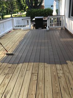 a wooden deck with a mop on it next to a white fence and trees