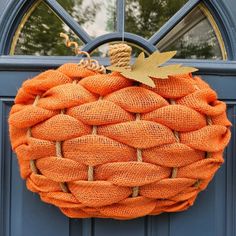 an orange burlock wreath hanging on a blue door with a gold acorn