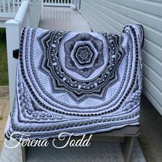 a crocheted blanket sitting on top of a bench next to a white house