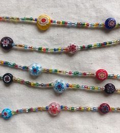 five colorful beaded necklaces are lined up on a white tablecloth, one is multicolored and the other has flowers