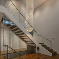 a white staircase with glass railing and chandelier hanging from it's ceiling